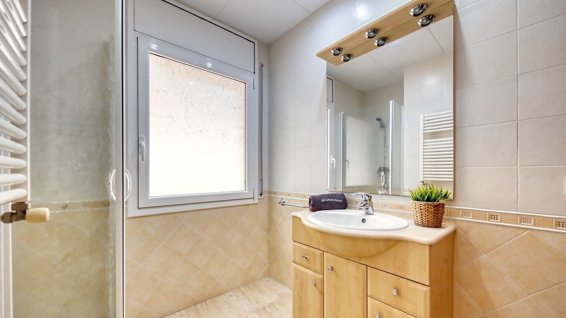 A bathroom with a window, a sink, a mirror, and a shower.