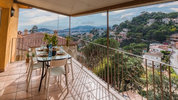 Un balcon avec une table dressée pour deux personnes, donnant sur un quartier résidentiel avec des maisons et des arbres.