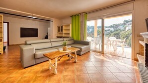 A living room with a sofa, a coffee table, and a TV. There is a balcony with chairs and a view of the city. - Villa 'Costacabana -  Marysol' with Sea View, Private Pool and Wi-Fi (Lloret de Mar)