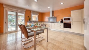 Une cuisine moderne avec un coin repas, comprenant une table en verre, des chaises et une vue à travers la porte-fenêtre coulissante.
