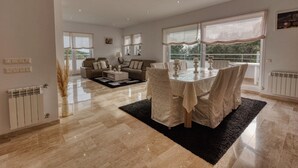 A spacious living area with a dining table, sofas, and a view through large windows.
