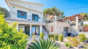 Una casa a due piani con un balcone, un muro in pietra e un giardino con diverse piante.