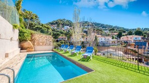 A swimming pool with blue water, surrounded by a grassy area with blue lounge chairs. - Villa 'Costacabana - Donna' with Sea View, Private Pool and WiFi (Lloret de Mar)