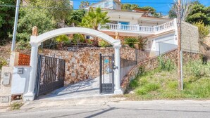 A gated entrance with a stone wall, a metal gate, and a white archway leading to a building with a balcony.