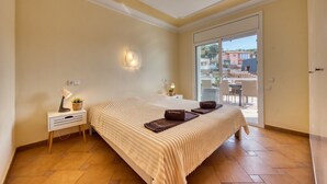 A bedroom with a bed, bedside table, lamp, and a view of the outside.