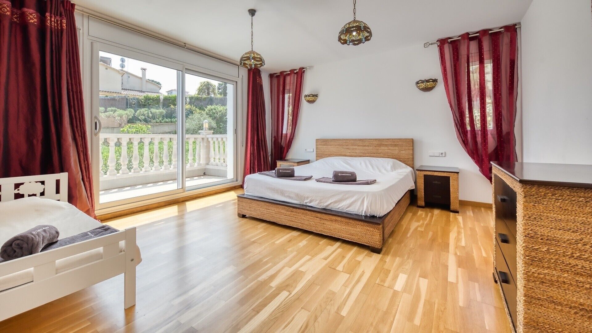 Un dormitorio con un ventanal grande, una cama, una mesita de noche y una lámpara de noche pequeña.
