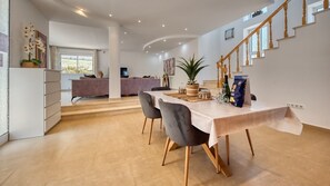 Een moderne eetruimte met een tafel gedekt voor twee personen, een trap en uitzicht op de woonkamer.