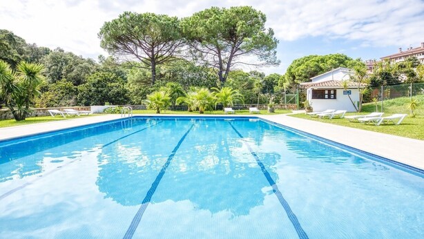 A swimming pool with clear blue water, surrounded by greenery and a small building.