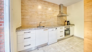 Una cocina con armarios blancos, encimera de granito, pileta de acero inoxidable, campana extractora y cafetera.