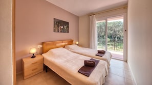 A hotel room with two beds, a nightstand, a lamp, a painting on the wall, and a balcony with a view. - Villa "Costacabana - Lloret" with Shared Pool, Private Terrace & Wi-Fi (Lloret de Mar)
