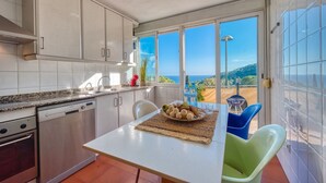 A kitchen with a dining area, a view of the sea, and a table set with food. - Villa "Costacabana - Santa Cristina" with Sea View, Only Families (Blanes)