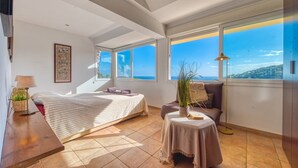 A bedroom with a bed, a bedside table, a lamp, a potted plant, a sofa, and a view of the sea. - Villa "Costacabana - Santa Cristina" with Sea View, Only Families (Blanes)