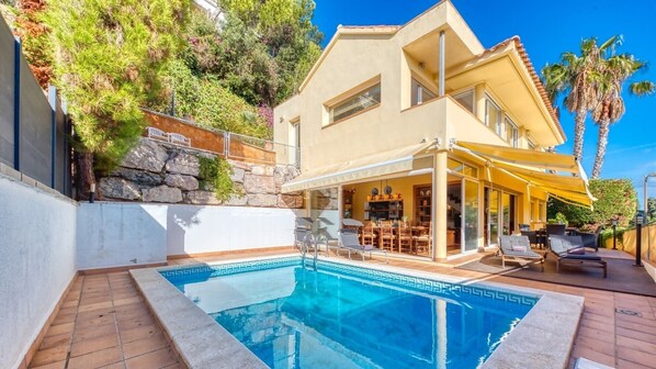 A modern house with a swimming pool, outdoor seating, and a stone retaining wall.
