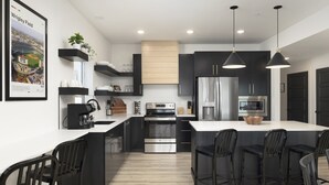 A modern kitchen with a large island, black cabinetry, stainless steel appliances, and pendant lighting. - 8 bdrm / 4000+ sqft home w/ golf simulator, outdoor sauna, hot tub & lake views! (HOLLISTER)