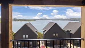 A view of a lake from a wooden balcony with three dark-colored buildings in the foreground. - 8 bdrm / 4000+ sqft home w/ golf simulator, outdoor sauna, hot tub & lake views! (HOLLISTER)