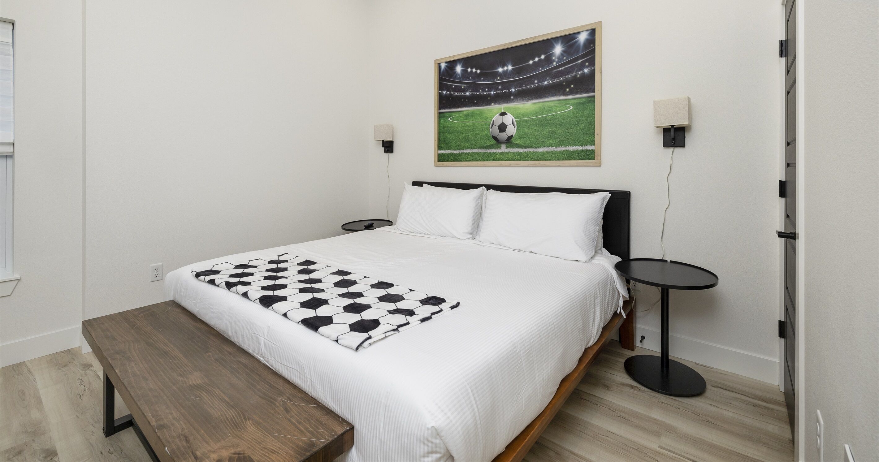 Un dormitorio con una cama, un banco, un cuadro en la pared y dos mesitas de noche.