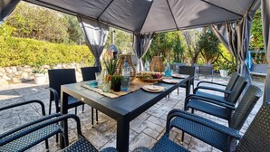 An outdoor dining area with a table set for six, surrounded by wicker chairs, under a large canopy. - Villa "Costacabana - Summertime" with Private Pool & Wi-Fi (Lloret de Mar)