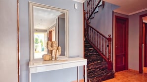 A hallway with a large mirror, a console table with decorative items, a staircase with wooden railings, and a door. - Villa "Costacabana - Summertime" with Private Pool & Wi-Fi (Lloret de Mar)