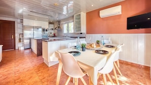 A modern kitchen with white cabinetry, a central island, and a dining area with white chairs and a table set for two. - Villa "Costacabana - Summertime" with Private Pool & Wi-Fi (Lloret de Mar)