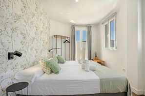 Une chambre avec deux lits, une lampe fixée au mur, une petite table et une fenêtre avec des rideaux.