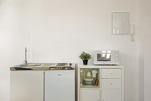 Une petite cuisine équipée comprenant un évier, une cuisinière, un four à micro-ondes et un petit placard contenant de la vaisselle.