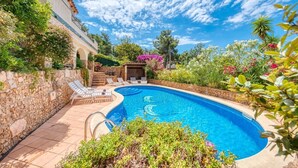 A swimming pool with a stone wall, lounge chairs, and a garden with various plants and flowers. - Villa "Costacabana -  Cleo" with Sea View, Private Pool & Wi-Fi (lloret de mar)