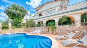 A pool with lounge chairs, a stone wall, and a two-story building with arches. - Villa "Costacabana -  Cleo" with Sea View, Private Pool & Wi-Fi (lloret de mar)