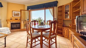 A living room with a fireplace, a dining table with chairs, a television, and a view through a large window. - Villa "Costacabana -  Cleo" with Sea View, Private Pool & Wi-Fi (lloret de mar)