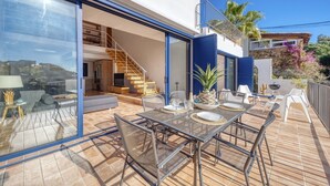 A modern outdoor dining area with a table set for two, a sofa, and a staircase leading to an upper level. - Holiday Home "Costacabana - Casa Adora" with Mountain View, Shared Pool & Wi-Fi (Tossa de Mar)