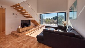 A modern living room with a TV, sofa, coffee table, and a staircase. - Holiday Home "Costacabana - Casa Adora" with Mountain View, Shared Pool & Wi-Fi (Tossa de Mar)
