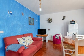 Un salon avec un canapé rouge, un téléviseur, une petite table et un réfrigérateur blanc.