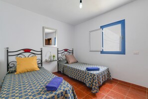 Une chambre avec deux lits, un miroir, une fenêtre à cadre bleu et une petite table recouverte d’une nappe bleue.