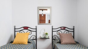 Une chambre avec deux lits, chacun agrémenté de draps à motifs, une petite étagère avec une plante et un miroir au mur.