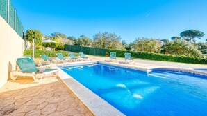 Ein Schwimmbecken mit Liegestühlen, einer gefliesten Terrasse und einer Hecke im Hintergrund.