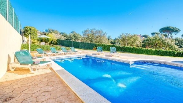 A swimming pool with lounge chairs, a tiled deck, and a hedge in the background.