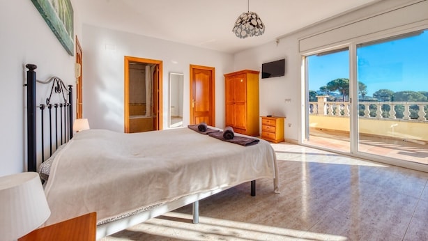 Ein Schlafzimmer mit einem großen Bett, einem Holzschrank, einem Fernseher und einem Balkon mit Blick.