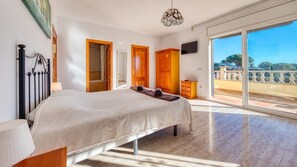 A bedroom with a large bed, a wooden wardrobe, a television, and a balcony with a view.