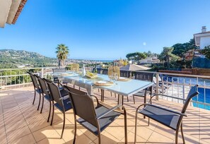 Une terrasse avec une table et des chaises, donnant sur une étendue d’eau et une ville située au loin.