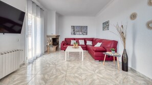 Un salon avec un canapé rouge, une table basse blanche, une cheminée et un téléviseur fixé au mur.