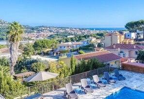 A pool area with lounge chairs and a view of a coastal cityscape.