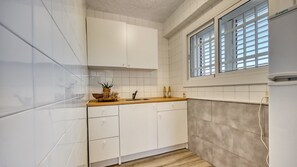 Une cuisine avec des meubles blancs, un plan de travail en bois, une fenêtre avec des stores et un four encastré.