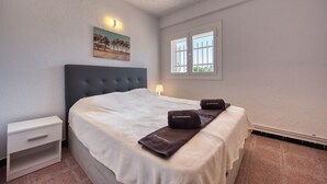 A bedroom with a bed, a nightstand, a lamp, a window, and a painting on the wall. - Villa "Costacabana - Abigail" with Sea View, Private Pool & Wi-Fi (Lloret De Mar)