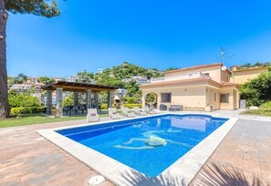Una piscina con sillas de descanso, una pérgola y un edificio con tejado de baldosas.