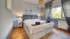 A bedroom with a large bed, bedside tables, a chandelier, and a window with curtains. - Villa "Costacabana - Yara" with Private Pool & Wi-Fi (Lloret De Mar)