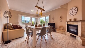 A modern living room with a dining area, a fireplace, and a large window overlooking a scenic view. - Villa "Costacabana - Yara" with Private Pool & Wi-Fi (Lloret De Mar)