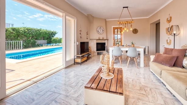 A spacious living room with a large window, a pool, a dining area, and a fireplace. - Villa "Costacabana - Yara" with Private Pool & Wi-Fi (Lloret De Mar)