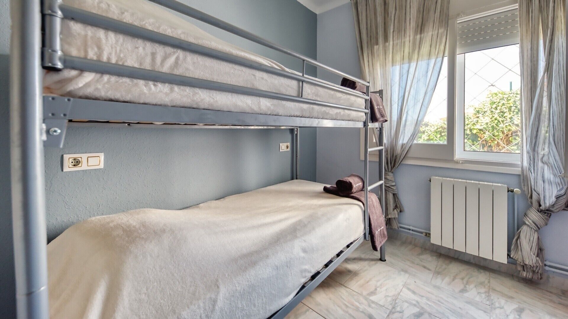 A bunk bed room with a window, curtains, and a radiator.