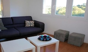 A modern living room with a dark sofa, a white coffee table, and two grey ottomans.