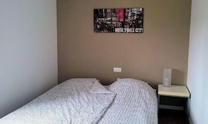 A single bed with a patterned bedspread, a wall-mounted picture of New York City, and a bedside table with a tissue box.