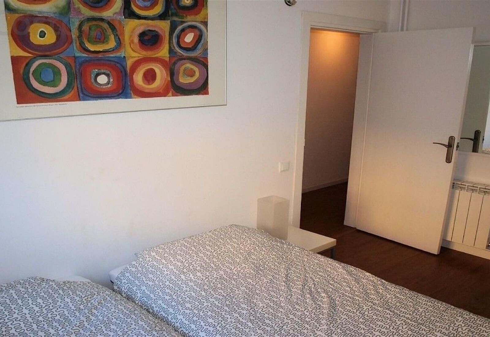 A bedroom with a bed, a small bedside table, and a colorful abstract painting on the wall.